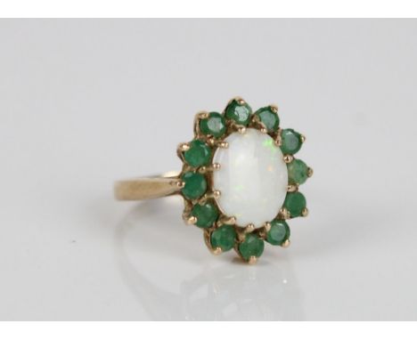 9ct gold opal and emerald cluster ring, the cabochon white opal surrounded by a halo of emeralds in basket setting on plain b