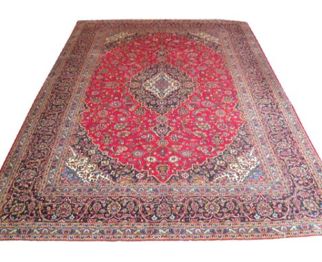 FINE KASHAN CARPET, 384cm x 292cm, midnight blue pole medallion on a ruby field of scrolling vines and palmettes inside tripl