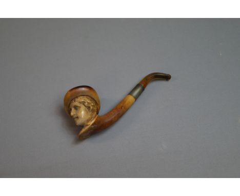 A carved meerschaum pipe with amber mouthpiece, the bowl in the form of a boy wearing a hat