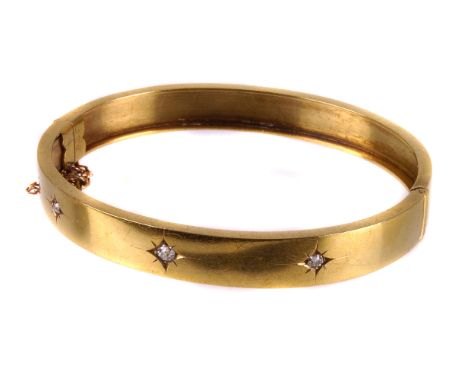 A Victorian yellow metal and diamond bangle, the plain oval hinged bracelet set with three old cut stones in star mounts 