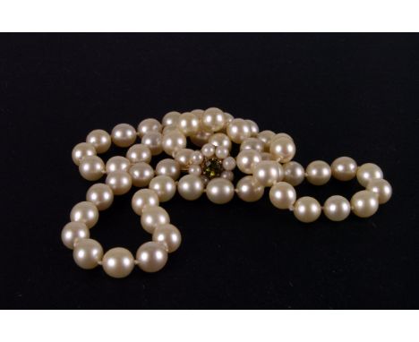 A single strand pearl necklace, the uniform white pearls on knotted cotton united by a 9ct gold clasp set with a peridot and 