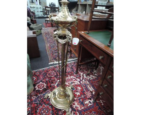 A late Victorian brass torchere/lamp stand having adjustable column with ornate ram's mask and foliate decoration and a brass