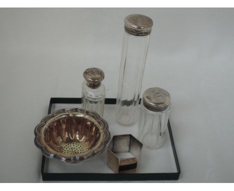 Three glass dressing table pots having HM silver lids, an HM silver napkin ring of hexagonal form and a white metal strainer 
