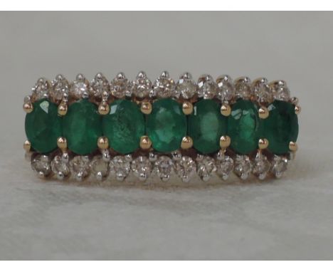 A ladies dress ring having a central row of seven oval cut emeralds flanked by two rows of diamond chips in a stepped claw mo