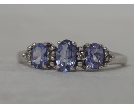 A ladies dress ring having three graduated tanzanite stones interspersed by diamond chips in a raised mount on a 9ct white go