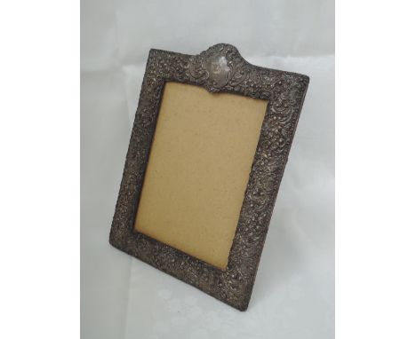A silver photograph frame of rectangular form having arch to top, extensive repousse floral and scroll decoration and leather