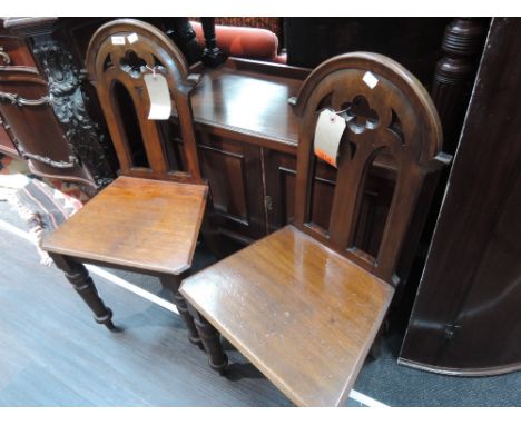 A pair of Victorian mahogany hall chairs of gothic design having arch backs with solid seats and turned legs