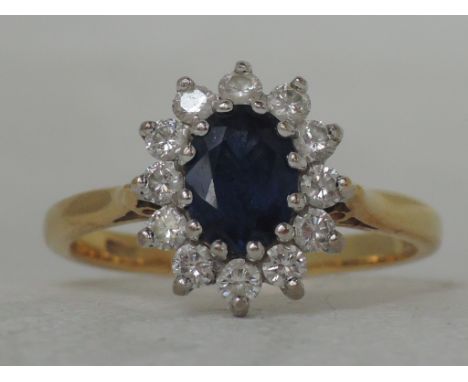 A ladies dress ring having an oval sapphire and diamond cluster in a basket claw mount to raised shoulders on an 18ct gold lo