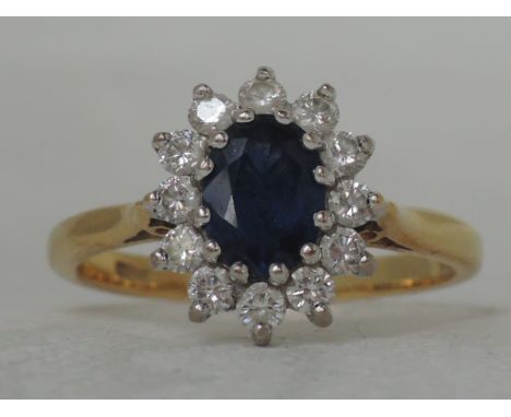 A ladies dress ring having an oval sapphire and diamond cluster in a basket claw mount to raised shoulders on an 18ct gold lo