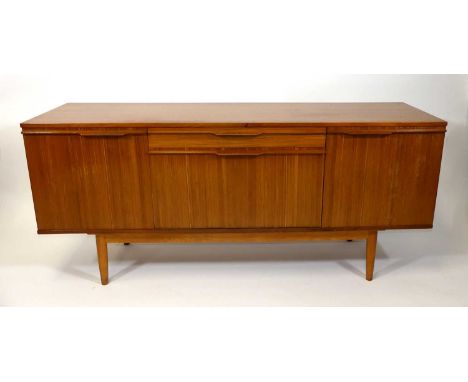 A 1960s teak sideboard, having a central baize-lined cutlery drawer over fall-front compartment flanked by cupboard doors, wi
