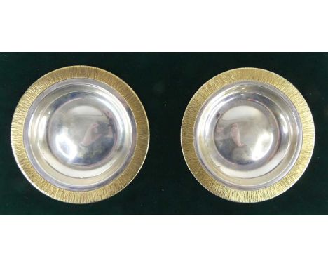 A pair of 1970s silver circular small alms dishes, each with raised naturalistic engine-turned gilt borders, housed in origin