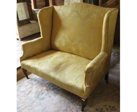 A circa 1900 upholstered wing back scroll arm two seat sofa on square tapered legs to castors