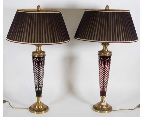 A pair of Bohemian ruby overlaid glass and lacquered brass table lamps with pleated silk shades, retailed by Art and Decors o