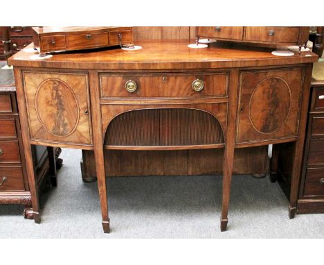 A George III Mahogany bow front sideboard, crossbanded, with tambour fronted cupboard and on square tapering supports. 147cm 