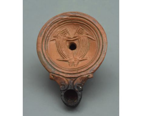 A terracotta oil lamp in deep red burnish finish; the discuss decorated with two cornucopias signifying the goddess Fortuna. 