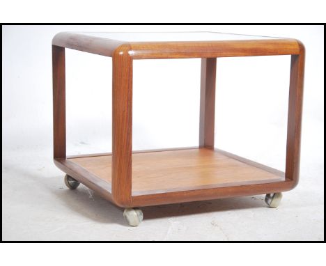 A good vintage G-Plan teak wood coffee table  of square form with glass top over lower shelf and raised on stepped castors to