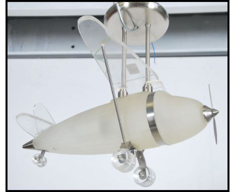 A contemporary frosted glass ceiling light in the form of an aeroplane being set to white metal brackets and ceiling mount