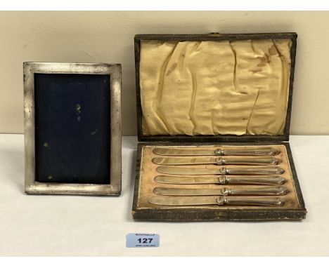 A silver photograph frame lacking glass, 6½' high and a cased set of six cake knives with loaded silver handles