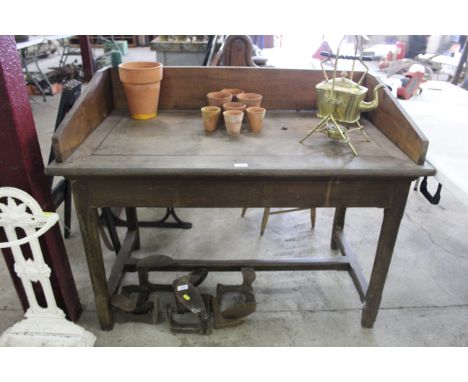 A pine garden potting table with a quantity of clay pots and tools hanging to the side