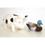 A small painted wooden decoy duck and a ceramic black and white pig