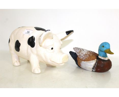 A small painted wooden decoy duck and a ceramic black and white pig
