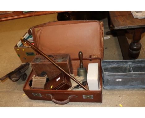 A vintage suitcase and contents to include a cast iron shoe last, bell, walking stick, small vintage case etc.