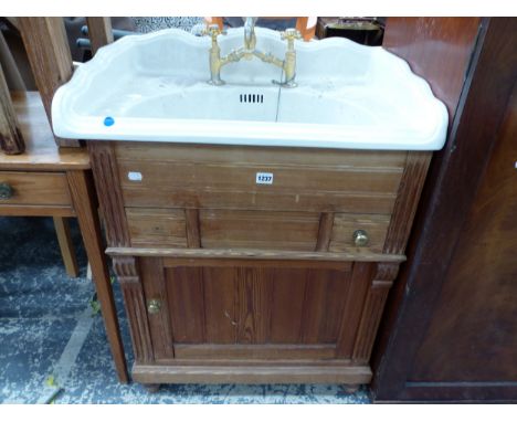 A CERAMIC WASH BASIN WITH GILT MIXER TAPS, THE PINE BASE WITH DRAWERS AND A DOOR BETWEEN FLUTED PILASTERS