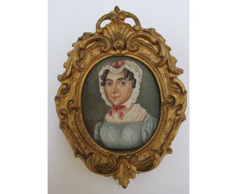 A 19TH CENTURY OVAL PORTRAIT MINIATURE OF A LADY IN A BLUE DRESS AND BONNET WITH RED RIBBONS, in a decorative oval gilt frame