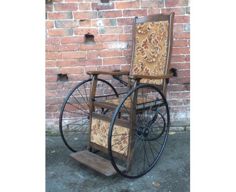 AN ANTIQUE OAK AND TAPESTRY SEAT INVALID CHAIR, with original spoked wheels