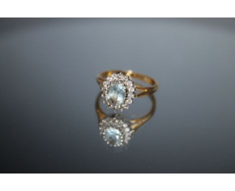 A HALLMARKED 18 CARAT GOLD DRESS RING, set with an aqua marine type stone and surrounded by sixteen diamonds, approx weight 4