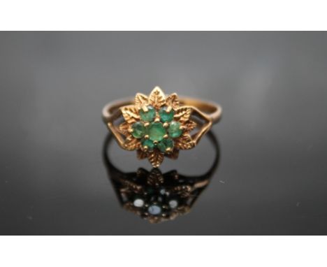 A HALLMARKED 9 CARAT GOLD EMERALD RING, having seven emeralds in a floral type setting, ring size U