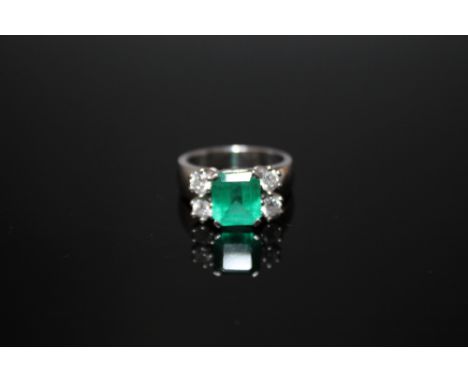 AN 18 CARAT WHITE GOLD EMERALD AND DIAMOND RING, set with an emerald cut emerald measuring approx 8mm by 7mm with two brillia