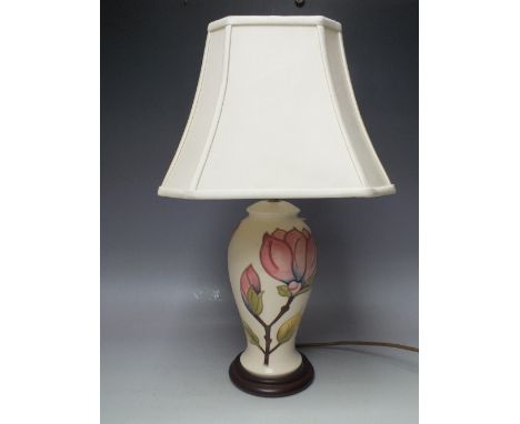 A MOORCROFT MAGNOLIA PATTERN TABLE LAMP, cream ground with typical tubelined decoration, raised on a circular wooden plinth, 