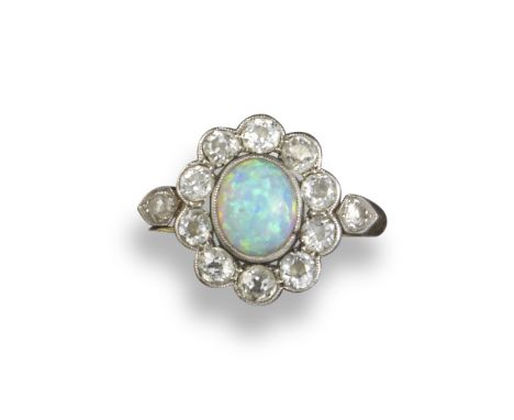 An Edwardian opal and diamond cluster ring, the solid white opal cabochon is millegrain-set within a surround of old cushion-