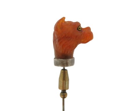 A carved amber dog's head stick pin, with glass eyes, set in silver, 8.7cm long