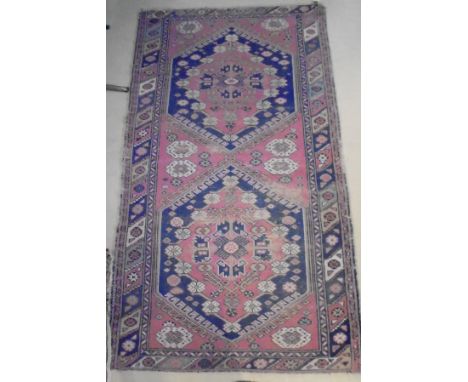 A Caucasian carpet, the central panel set with two lozenge shaped medallions on a pink ground with stylised flower head decor