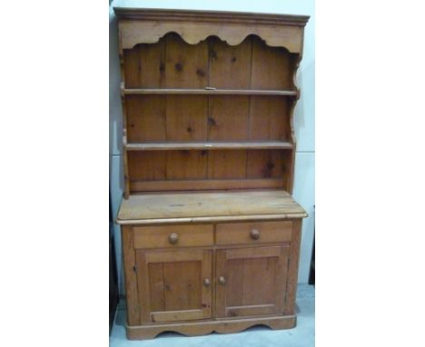 A pine dresser with two shelf plate rack over two drawers and two cupboard base on shaped plinth 105cm x 49cm x 183cm high