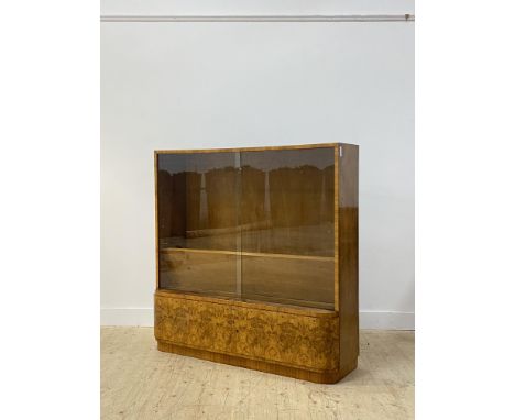 An Art Deco period walnut bookcase, the twin sliding glass doors enclosing two adjustable shelves (no shelf stays) above a dr