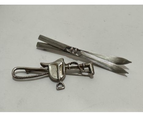 A 800 standard white metal pair of Skis brooch, (L x 8cm) and a silver saddle and whip brooch, (L x 6cm) (2)