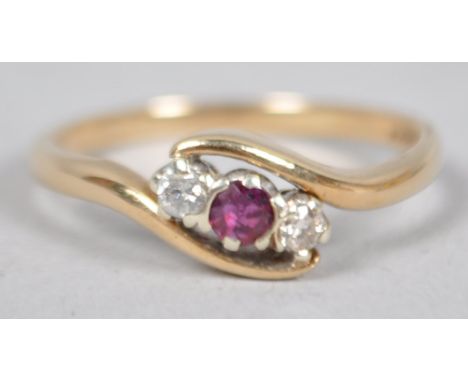 A yellow metal dress ring principally set with a round faceted cut ruby and flanked by two round brilliant cut diamonds. Hall