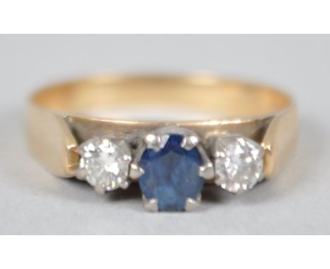 A yellow and white metal three stone ring. Principally set with an oval cut sapphire and flanked by two round brilliant cut d