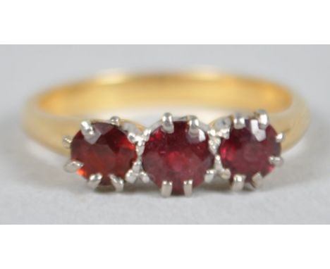 A yellow and white metal ring set with three round faceted cut garnets. No hallmark - stamped 18ct. Size: L 3.6 grams