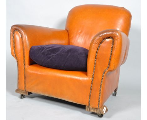 A club armchair, upholstered in tan leather with drop in purple velvet cushion, with studwork arms, on wooden feet and caster