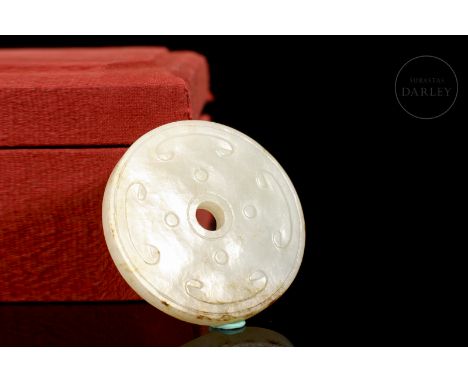 A jade disc carved in the shape of a ‘Bi’ with a small centred hole and a thin rim. Decorated with incised details of scrolls