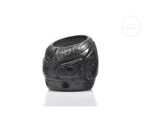 Archer ring made of dark green jade carved with bas-relief decorations. It has a rounded profile, which ascends generating an
