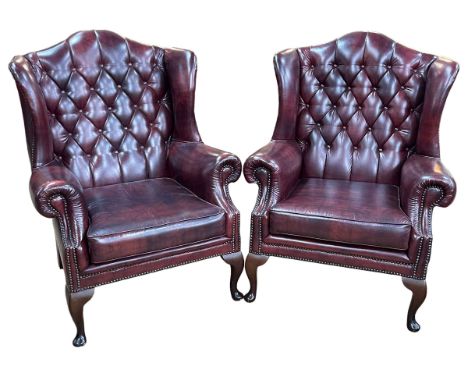 Pair ox blood button backed and brass studded wing armchairs.