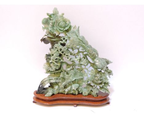 A 20th century jade carving, with a phoenix amongst peony and other flowers, on wood stand