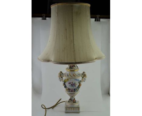 A CONTINENTAL CERAMIC TABLE LAMP, of urn form, decorated with ram's head mounts, floral encrusted, the ceramic stem 32cm high