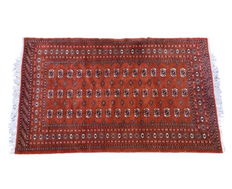 A 20th century Bokhara style rug, the brick red ground with three rows of fifteen Guls, within repeating guards and flag main