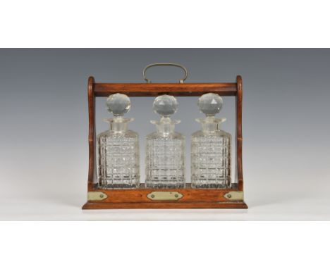 An Edwardian oak three bottle tantalus with plated mounts, fitted with three glass square section decanters with faceted glob